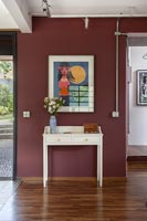 White console table and colourful artwork on dark red painted wall 