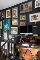 Black painted wall covered in framed pictures over wooden desk 