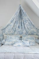 Blue and white fabric canopy over bed with matching cushions 