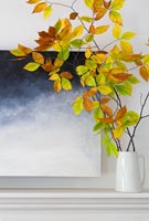 Branches filled with autumnal leaves in vase on mantelpiece 