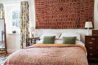 Patterned fabric wall hanging above bed in country bedroom 