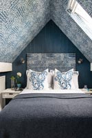 Modern bedroom with blue patterned wallpaper and matching headboard 