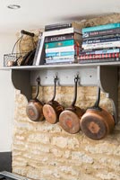 Copper pans on hooks under recipe books on shelf