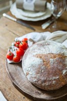 Loaf of uncut bread and tomatoes on rustic dining table 