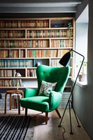 Green armchair next to window and bookshelves 
