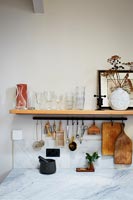 Marble worktop and wooden shelf with utensils in modern kitchen 