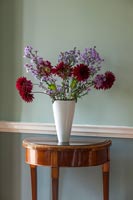 Red and purple flowers in white vase on antique console table 