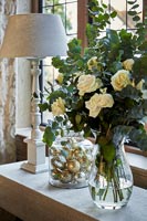 Flower arrangement and jar of gold Christmas baubles on stone table 