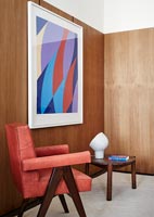 Red leather armchair, wooden walls and colourful artwork 