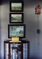 Glass display case and framed paintings on grey wall 