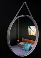 Contemporary bedroom seen through suspended circular mirror 