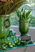 Glazed green pot of white tulips next to Christmas tree and tealights