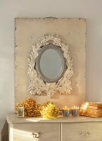 Plaster mirror on chest of drawers with dried flower heads and candles 