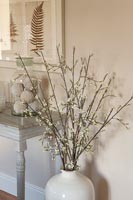 Large white vase of branches next to side table 