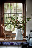 Reindeer ornament and jug of holly on country kitchen windowsill 
