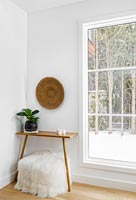 White fluffy foot stool and small wooden table next to window 