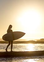 Woman standing on beach at sunset holding surfboard