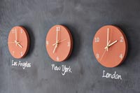 Orange wall clocks displaying different time zones on blackboard wall 