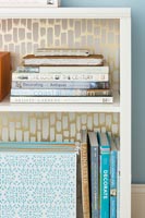 Bookcase backed with gold patterned wallpaper 