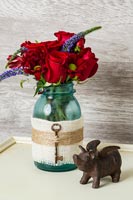 Red roses in glass jar decorated with hessian and an old key 