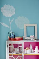 White painted flower on blue wall and pink lining inside sideboard cupboard 