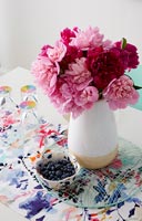 Pink and red flowers in ceramic vase on colourful table 