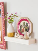 Pink flowers in vase on shelf with classic painting 