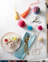 Pom poms and tassels on dining room table with cakes on plate 
