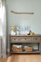 Macrame wall hanging over wooden sideboard decorated with pom poms 