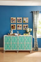 Framed photographs displayed on wall above colourful sideboard  