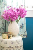 Pink flowers in cream coloured vase on bedside table 