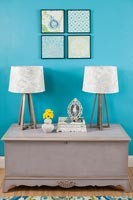 Blanket box with modern lamps next to blue painted wall 
