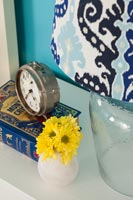 Small vase of yellow flowers and alarm clock on bedside table 