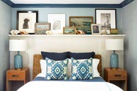 Wooden shelf of framed pictures above bed with rattan headboard 