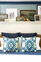 Shelf of framed paintings above bed with rattan headboard 