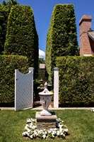 Stone urn lantern in formal garden with white wooden gate 