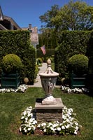 Lantern in formal garden with view through hedge to American flag on house 