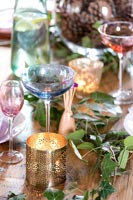 Coloured glasses and candle on dining table with decorative foliage 