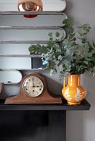 Stems of foliage in ceramic jug and vintage clock on mantelpiece 