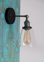 Sconce on wall with peacock feather patterned wallpaper 