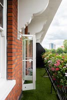 Artificial grass and planters of flowering plants on classic balcony 