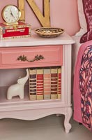 Books and ornaments on pink bedside table 