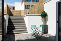 Green cafe table and chairs on modern terrace with split level garden