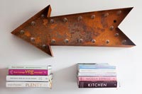 Rusted metal arrow shaped light artwork and books on floating shelves