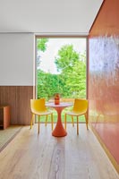 Orange table and yellow chairs next to orange wall 