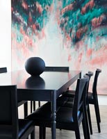 Black dining table and chairs with backdrop of modern artwork 