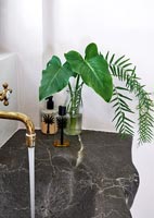 Vase of foliage next to marble sink with running water 
