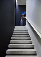 View up concrete staircase with black painted walls to colourful artwork