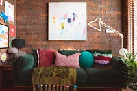 Large green sofa against exposed brickwork wall with framed painting 