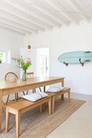 Wall mounted surfboard in white painted dining room with wooden furniture 